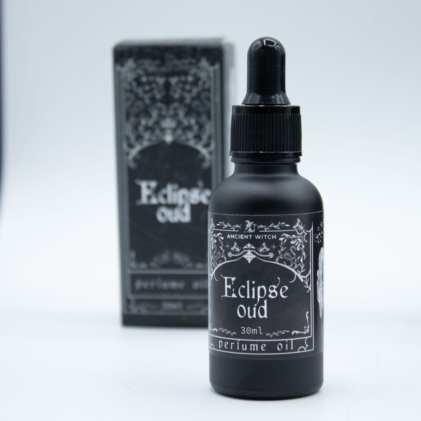 Black bottle of Eclipse Oud perfume oil with dropper and packaging on a light gray background