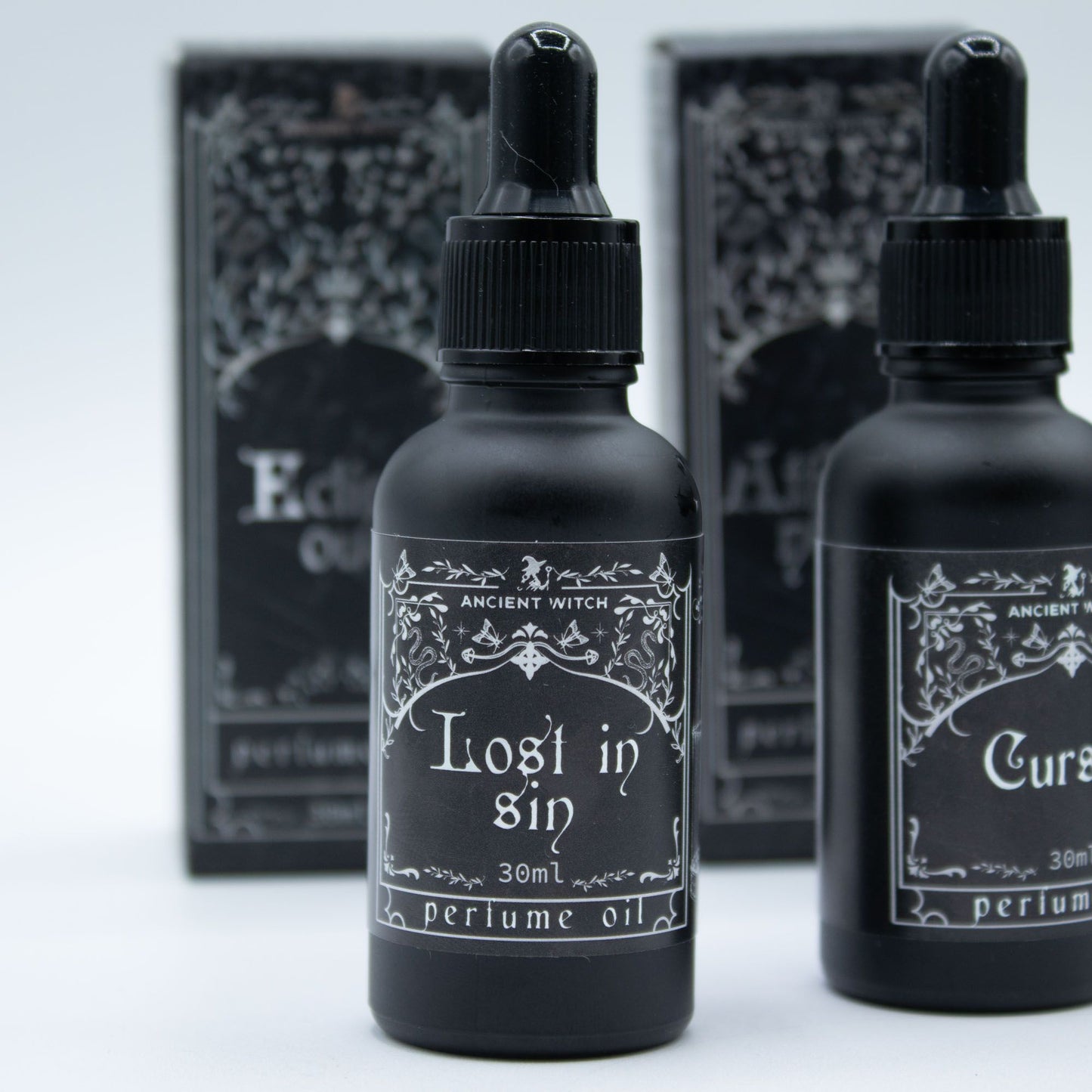 Two black perfume oil bottles with decorative labels on a light gray background.