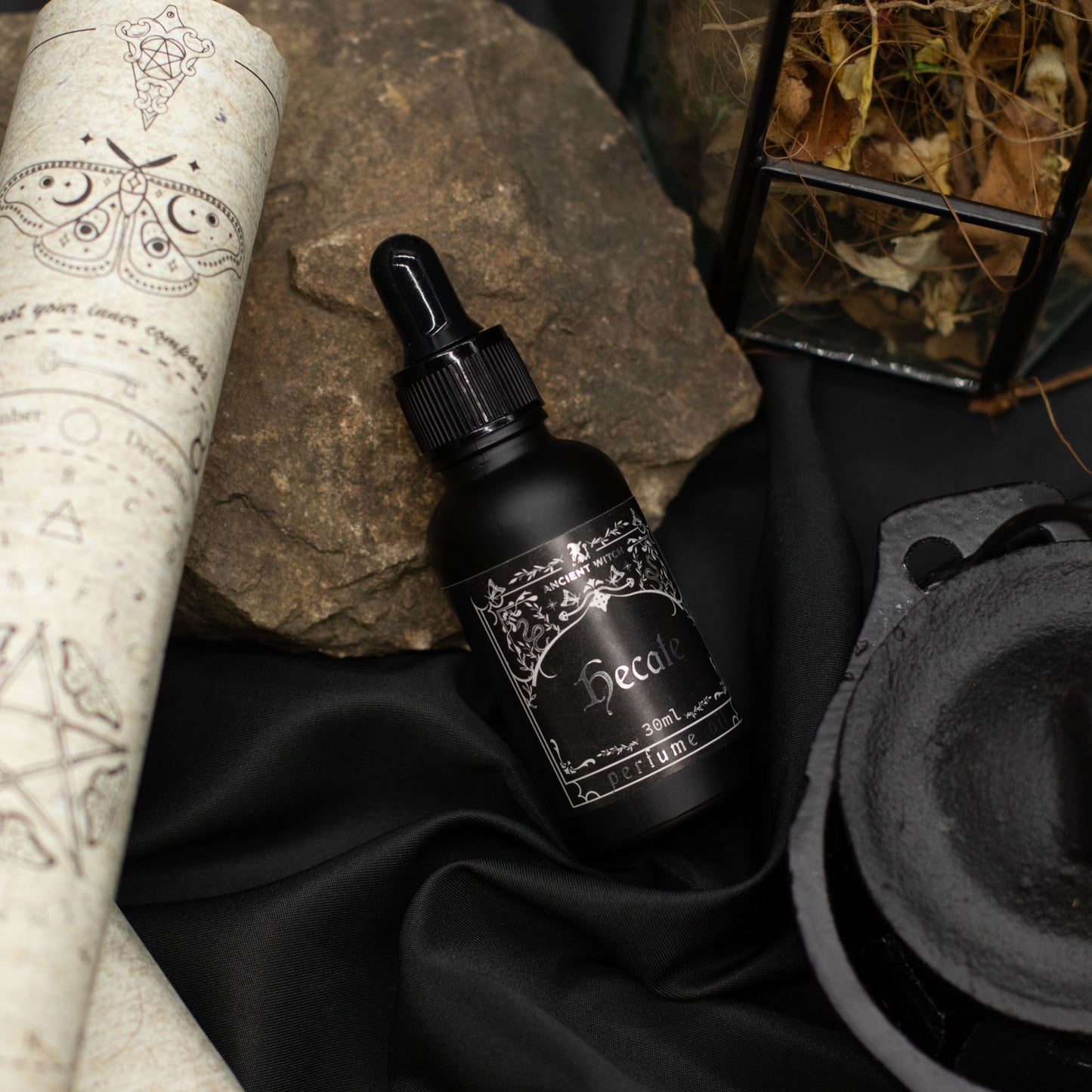 Black bottle with dropper labeled 'Hecate' on a dark fabric background