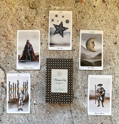 A set of tarot cards and a tarot box arranged on a rough stone surface. The center shows a boxed deck labeled 'Tranquility Tarot' with '128 Cards' on the front.