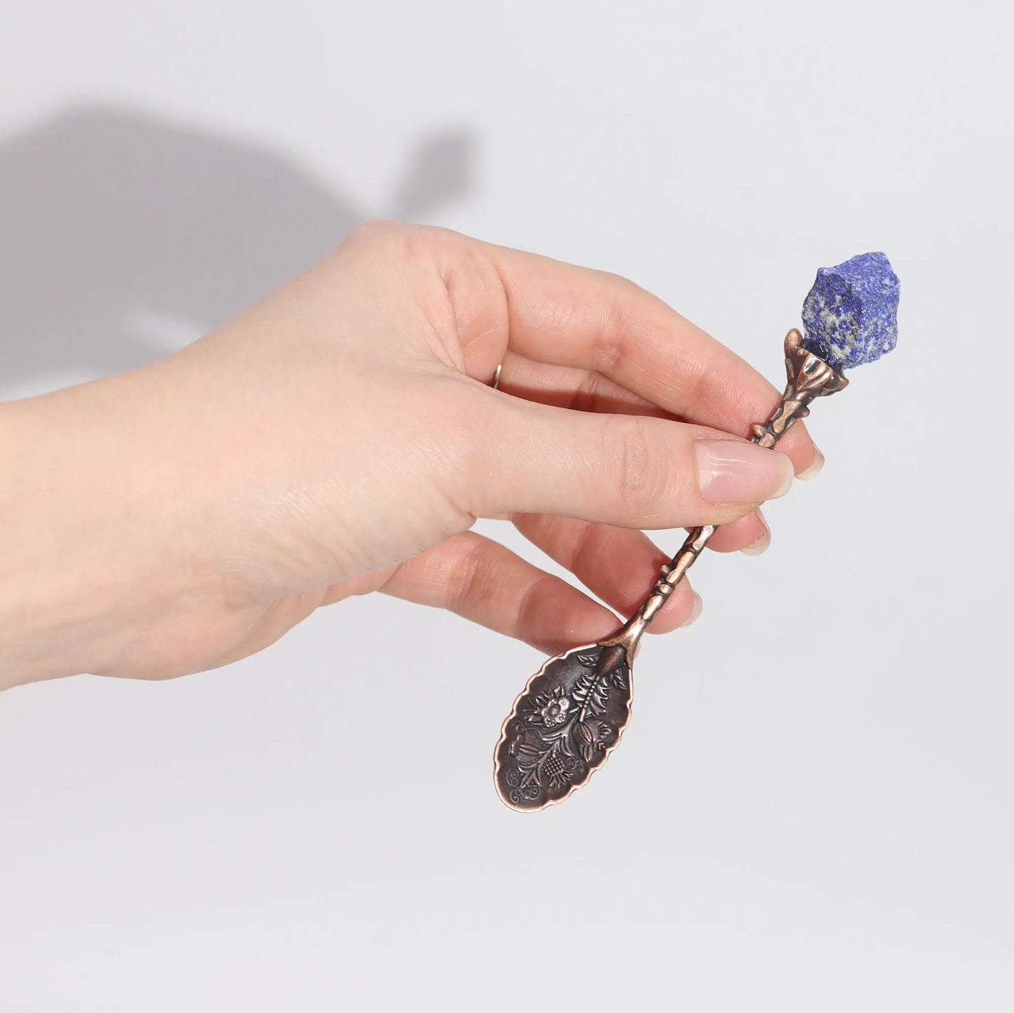 Hand holding a decorative spoon with a purple stone against a light background