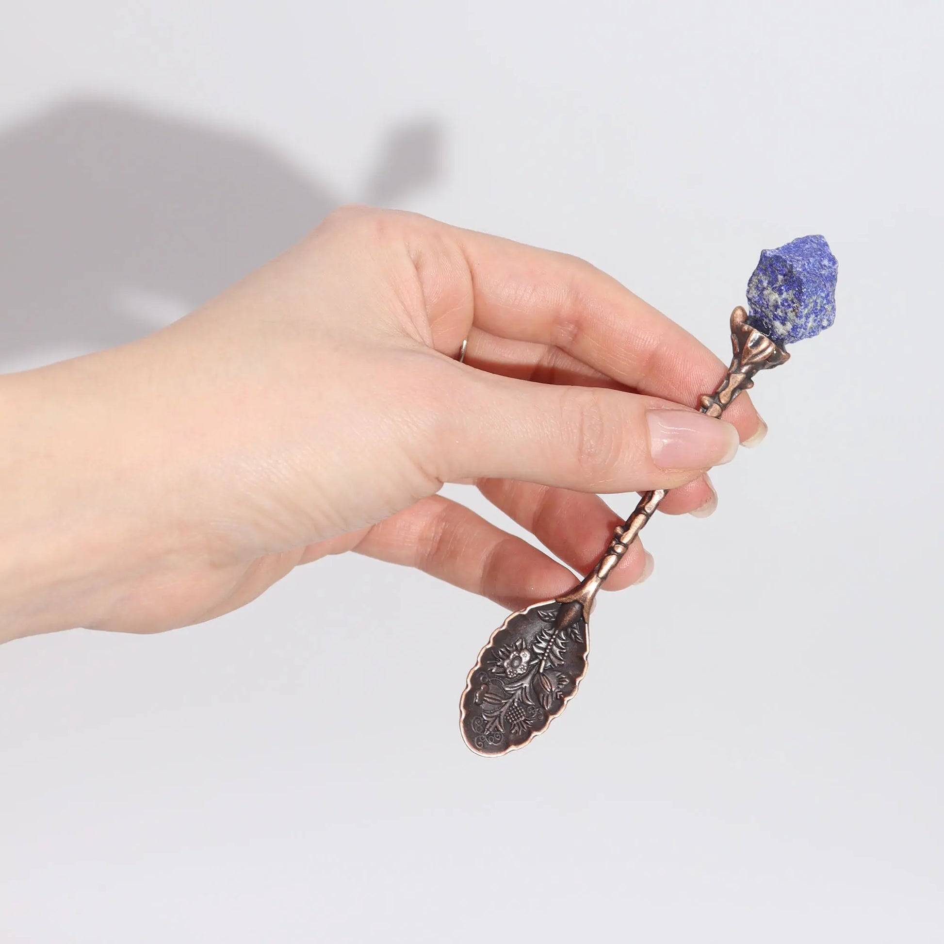 Hand holding a decorative spoon with a purple stone against a light background