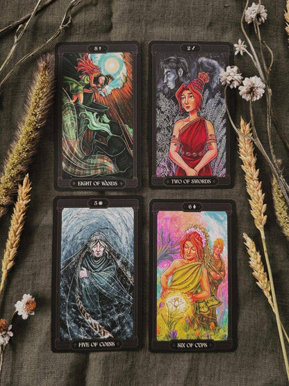 Four illustrated tarot cards arranged in a 2x2 grid on a dark textured fabric, surrounded by dried wheat stalks and small white flowers. The cards show fantasy artwork with titles including Eight of Wands, Two of Swords, Five of Cups, and Arc of Cups. Asphodelon Tarot by Asphodelon Studio featuring hand-painted Greek mythology artwork, gilded edges, premium matte cards and a deluxe gold foil presentation box.