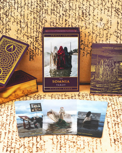 The Somnia Tarot cards and book on a textured surface with a mystical design.
