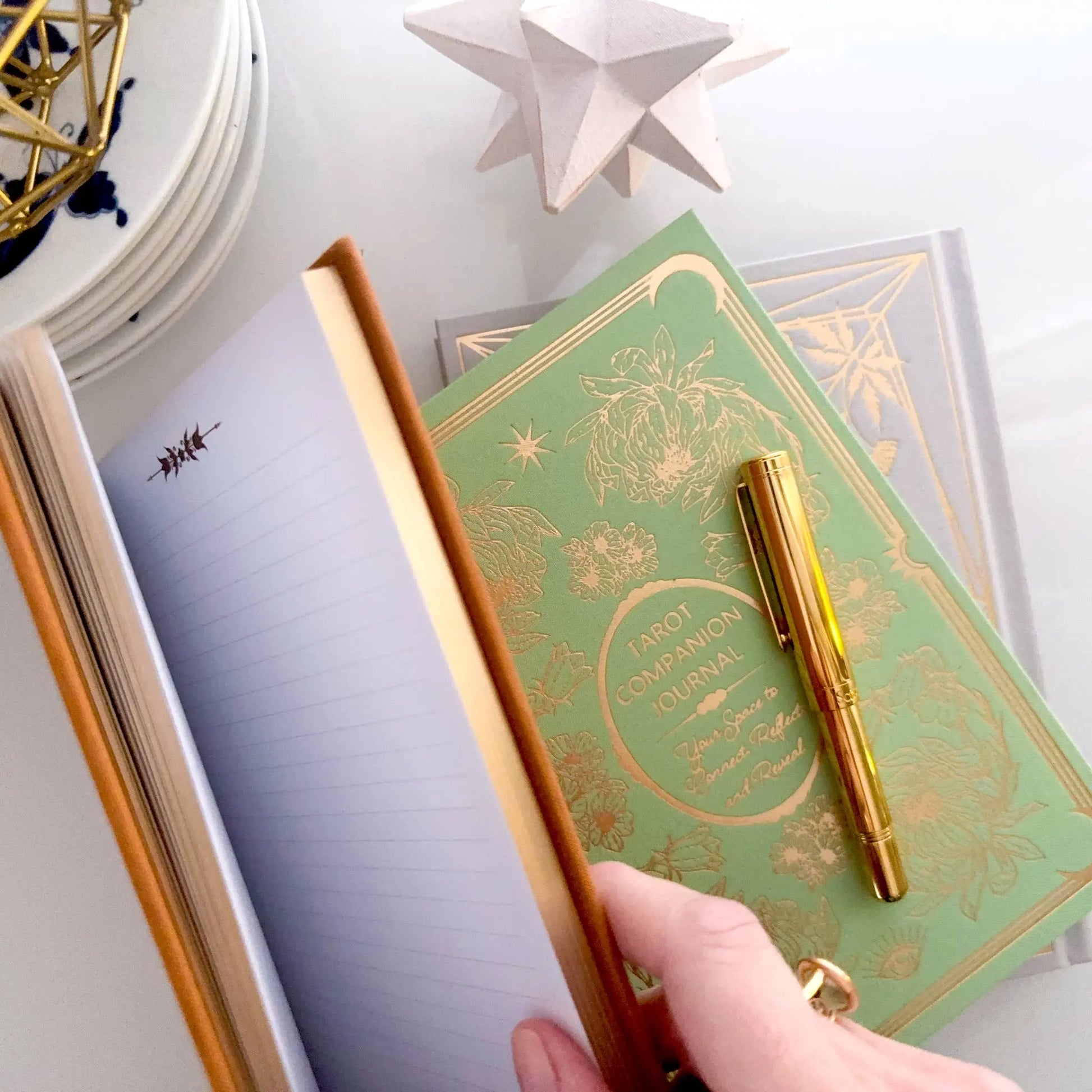 Green notebook with gold decorative elements and a matching pen on a white surface. Grimoire Bouchette and Co Oneness Emporium