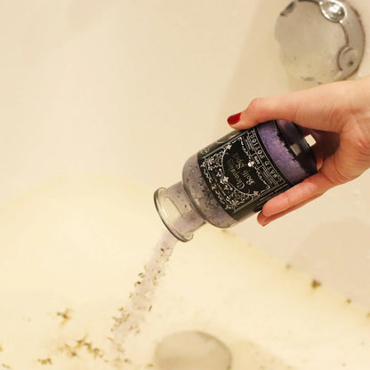 Hand holding a bottle of bath salt with a shower running in the background