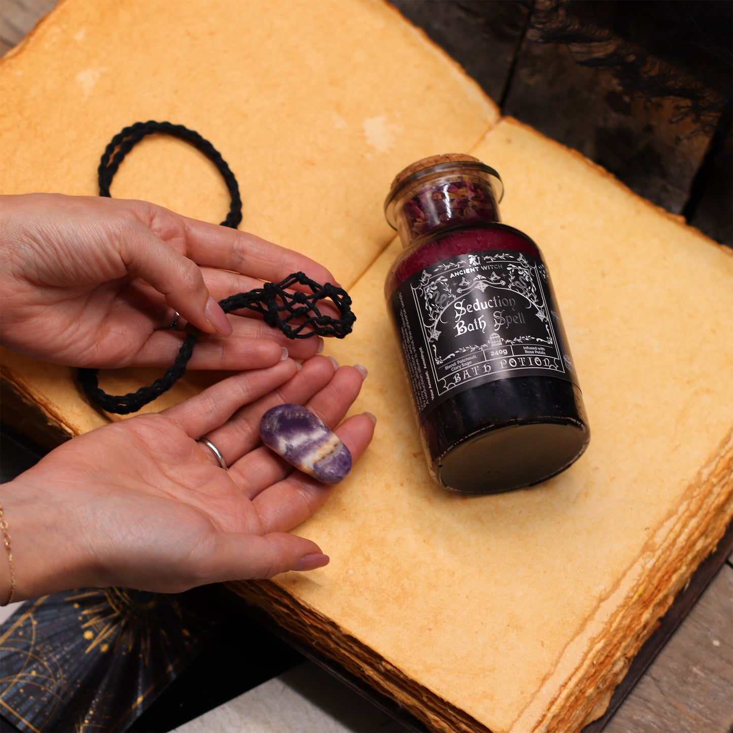 Hands holding a crystal ball, a bottle labeled 'Sorceress' on an old book