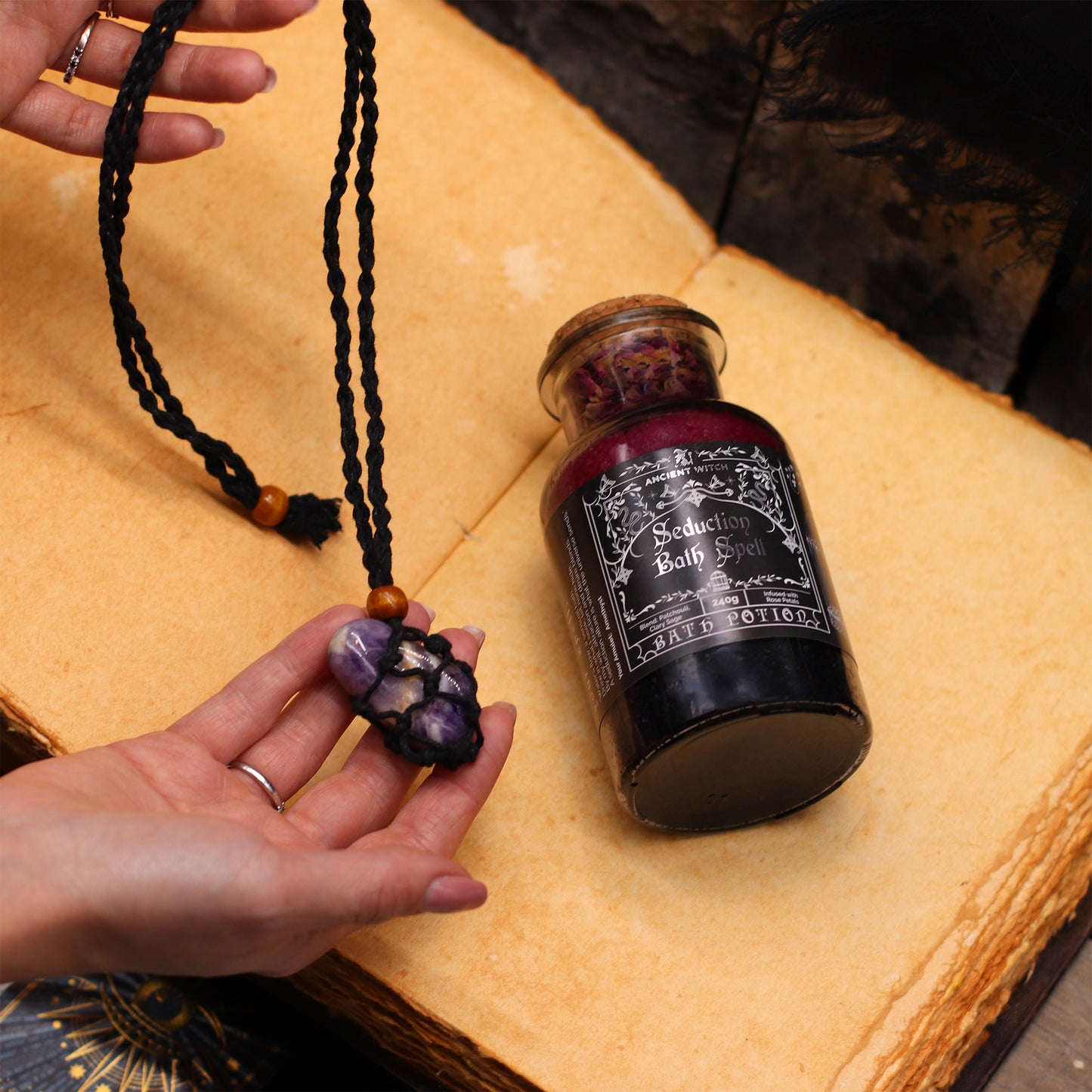 Hand holding a necklace with a bottle labeled 'Seduction Bath Salts' on a textured surface.