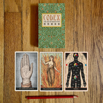 Codex: The Art of Divination book with three tarot cards on a wooden surface.