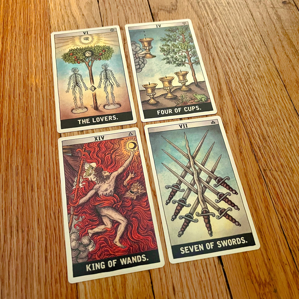 Four tarot cards laid out on a wooden tabletop: The Lovers, Four of Cups, King of Wands, and Seven of Swords.