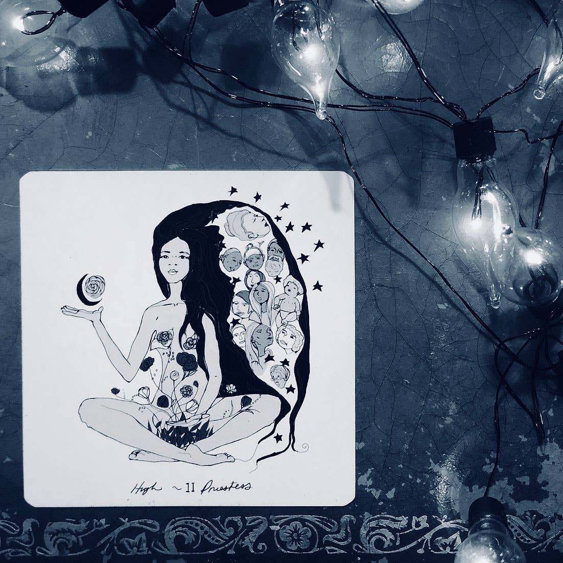 Illustration of a woman with floral designs on her hair and body, surrounded by string lights. Dark Days Tarot by Wren McMurdo Brignac featuring square black-and-white tarot cards inspired by the lunar cycle with a 180-page guidebook and collector's box.