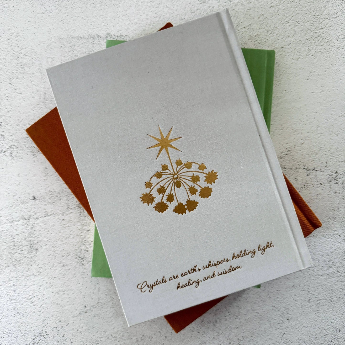 Stack of books with a gold star design and text on a textured surface Crystal companion journal by Bouchette and Co available from Oneness Emporium