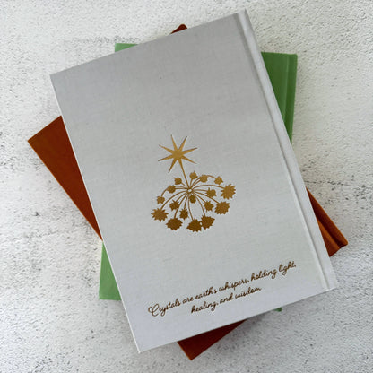 Stack of books with a gold star design and text on a textured surface Crystal companion journal by Bouchette and Co available from Oneness Emporium