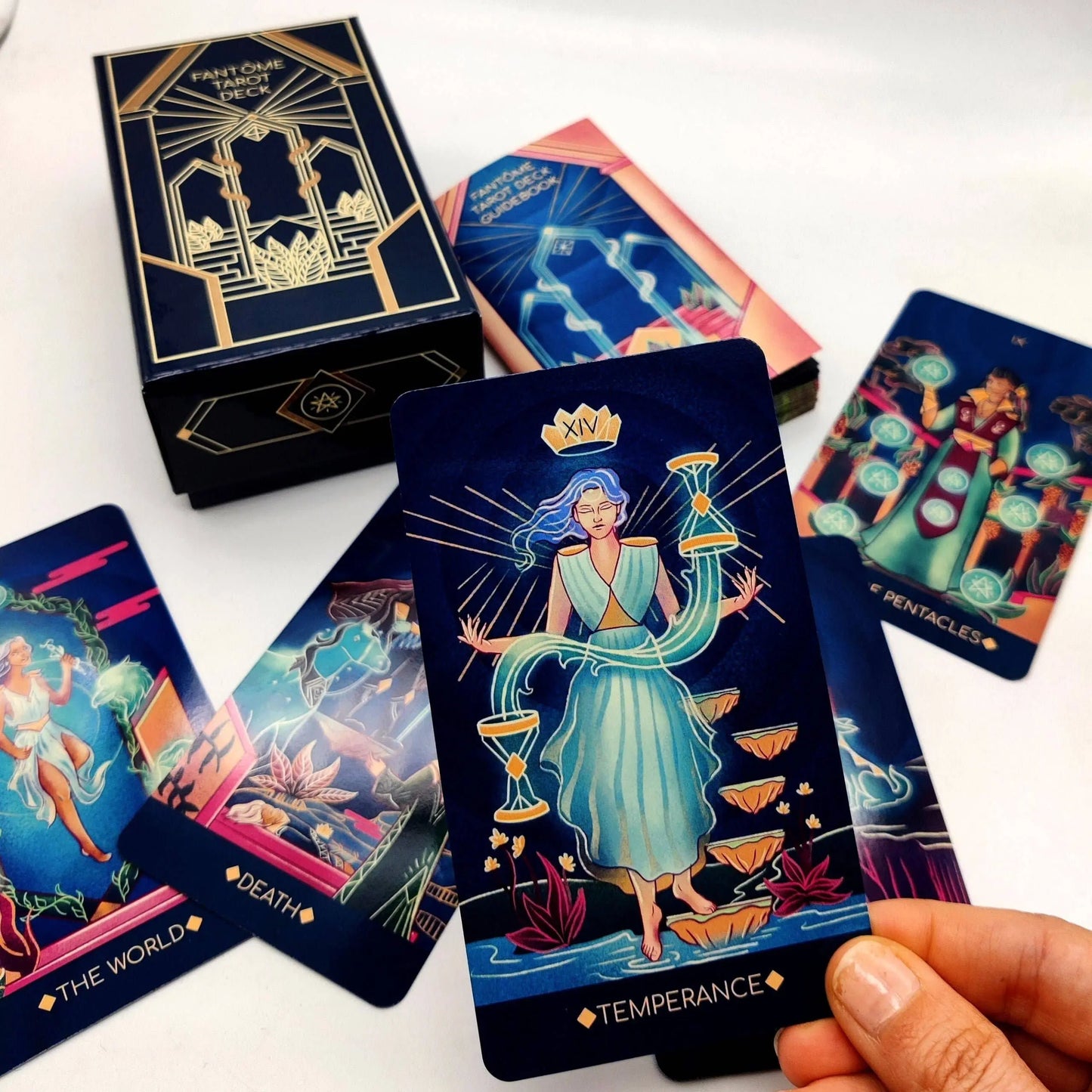 Collection of tarot cards with a focus on 'Temperance' card held by a hand, against a white background.