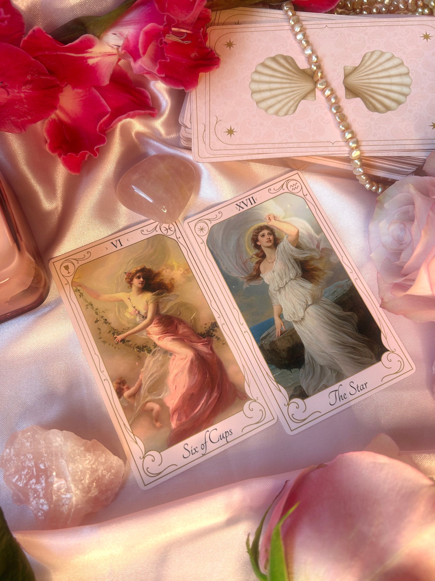 Two tarot cards featuring angelic figures on a soft pink fabric background with flowers and seashells. Six of cups and The star 