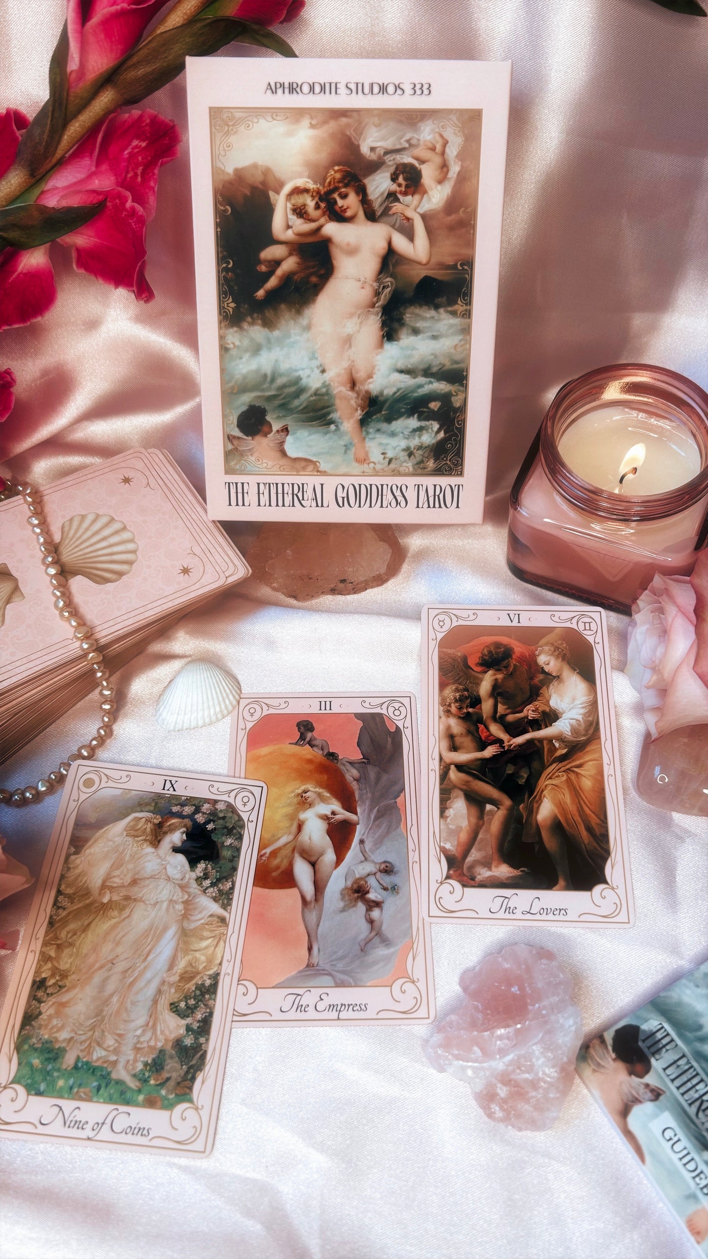 Tarot cards with artistic designs on a soft surface with candles and flowers.