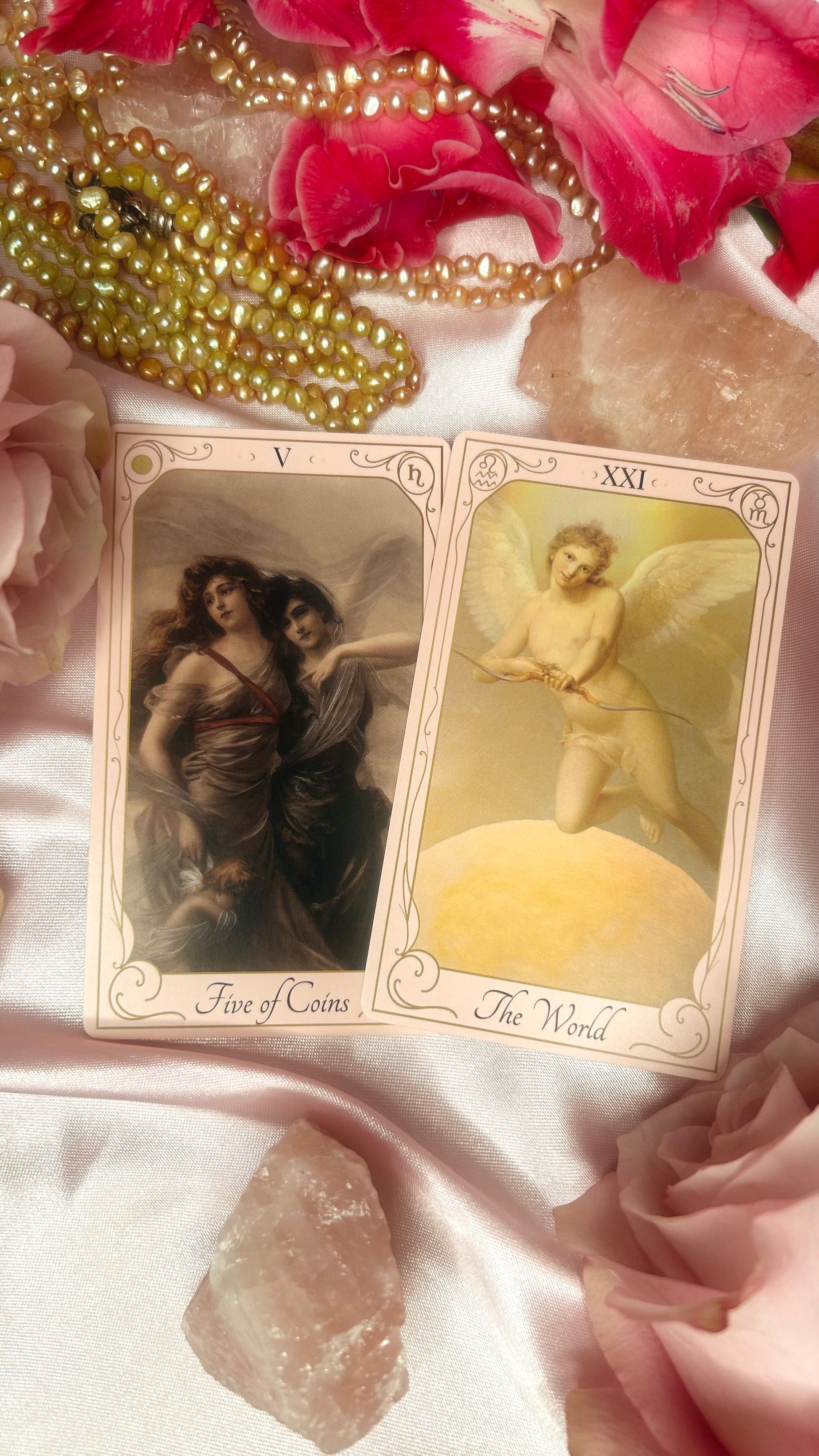 Two tarot cards with angelic figures on a pink fabric background with flowers and crystals.