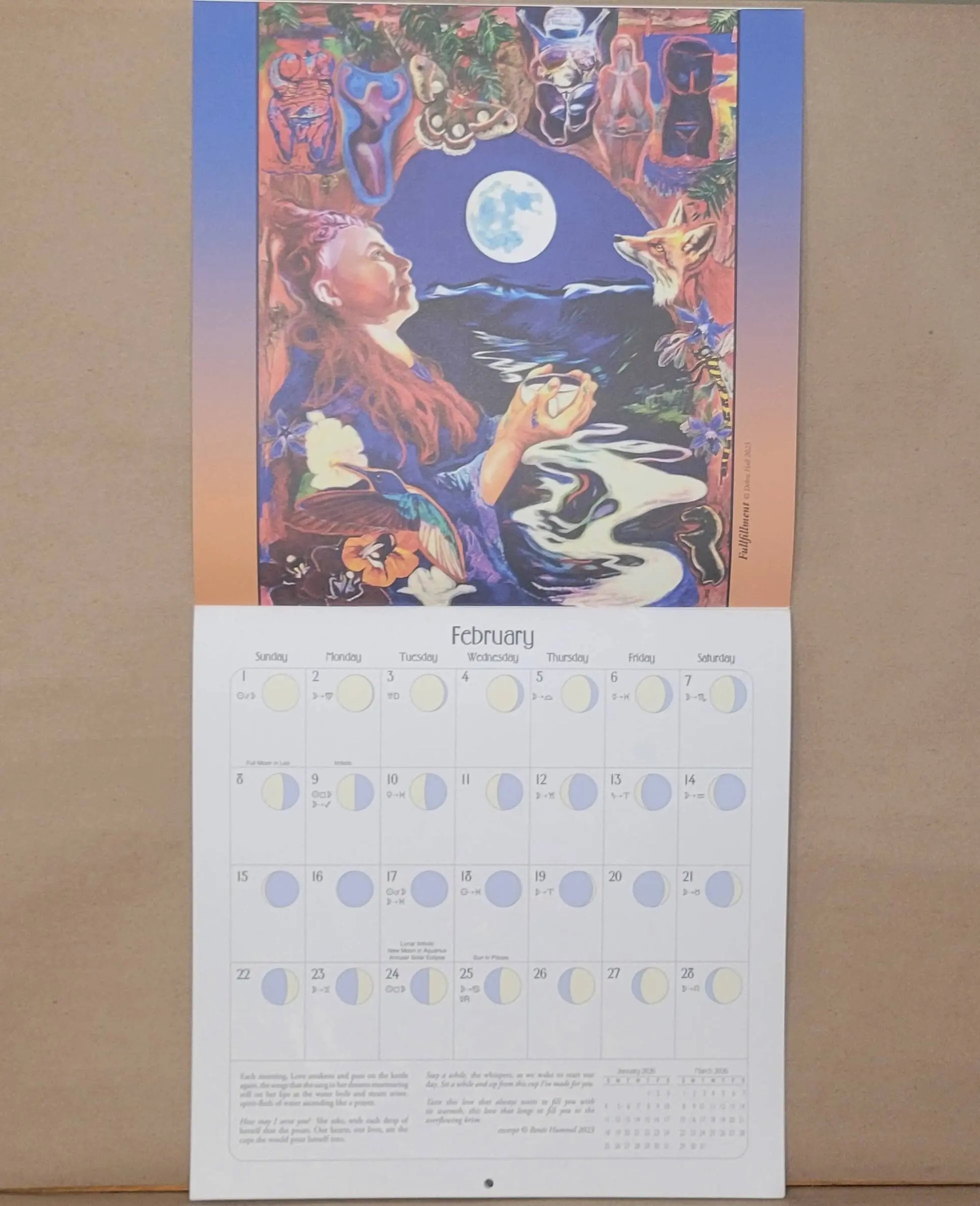 Calendar with a colorful illustration of a woman by a river and moon, on a wooden surface.
