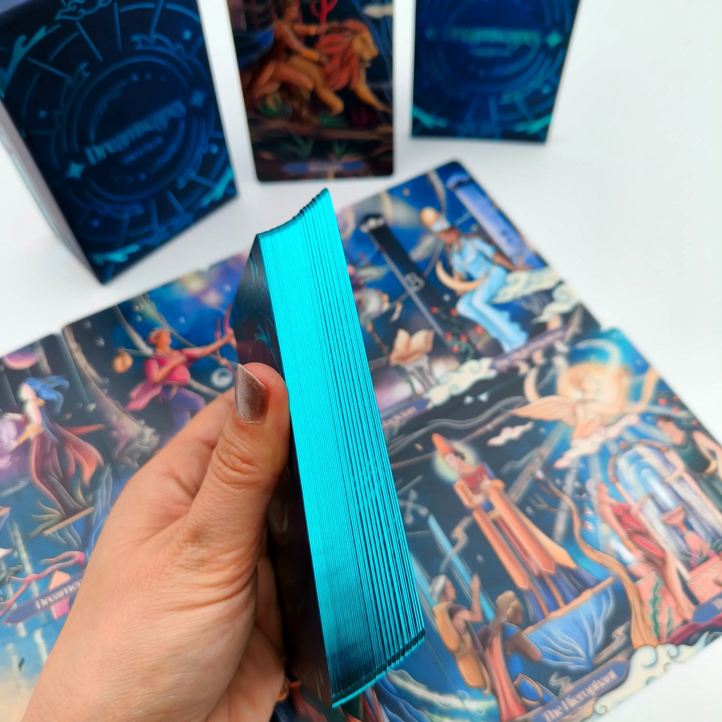 Hand holding a blue tarot card deck over tarot cards with colorful designs.