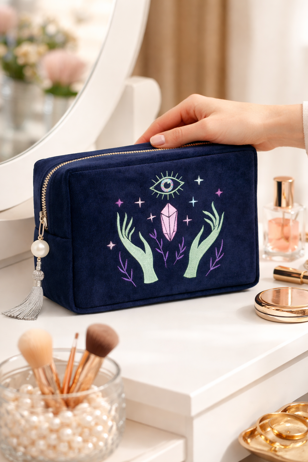 Navy makeup bag with mystical design held by a hand on a vanity table.