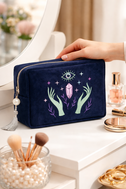 Navy makeup bag with mystical design held by a hand on a vanity table.