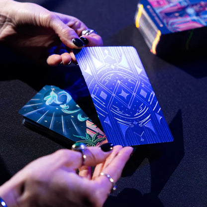 Hands holding tarot cards with intricate designs on a dark surface