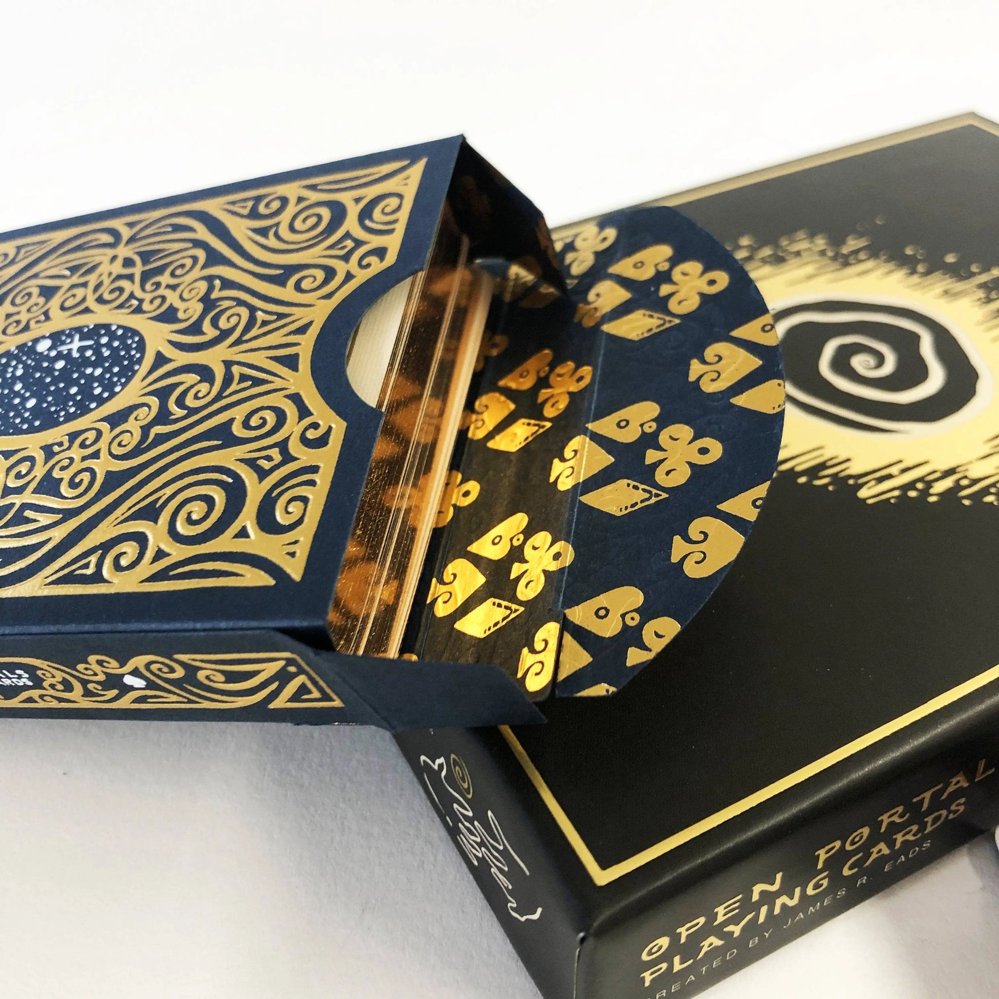Playing cards with gold designs on a black box labeled 'Open Portal Playing Cards' on a white background