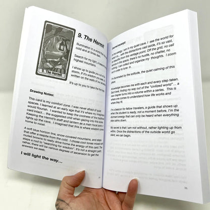 Open book with tarot card illustration and text held by a hand