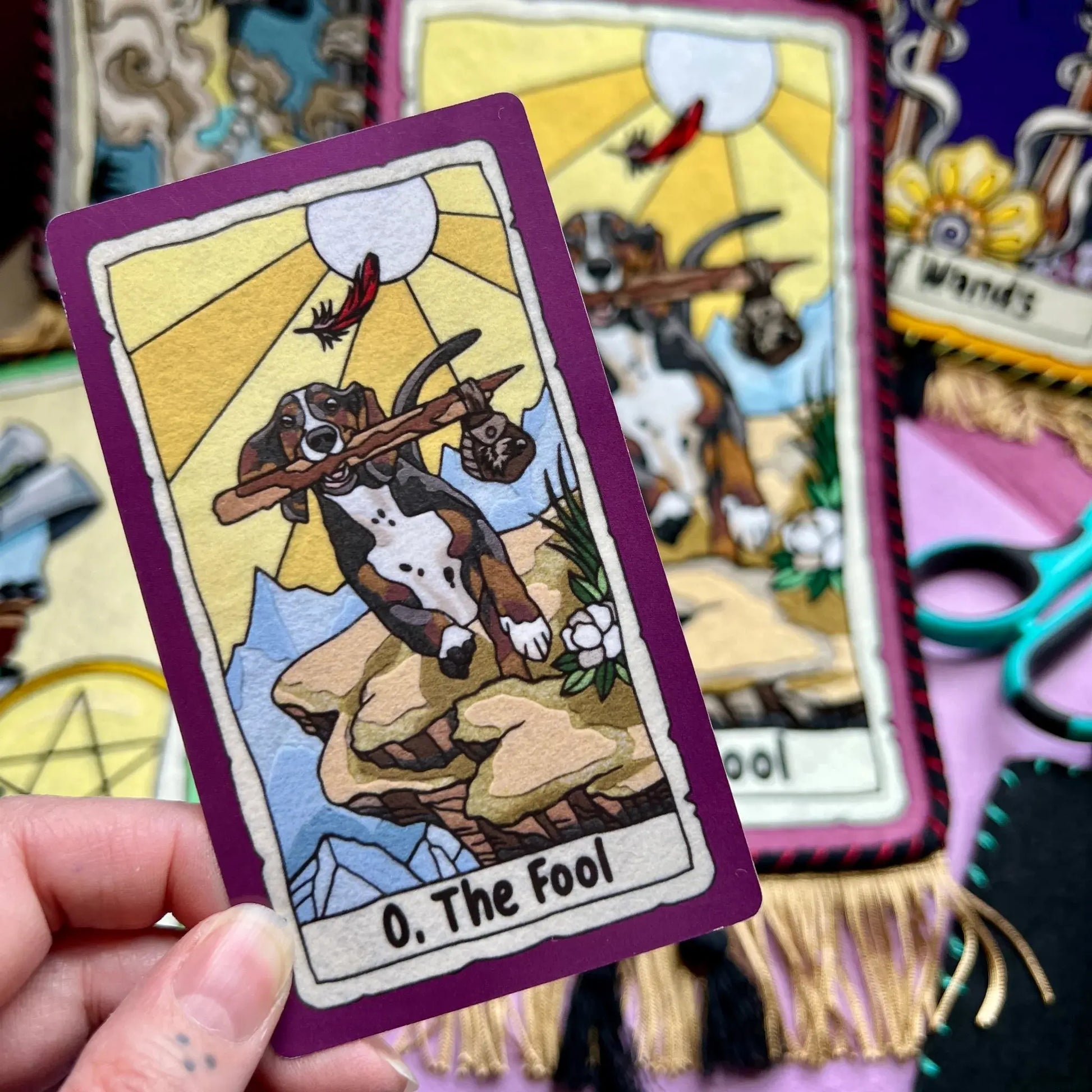Card from a tarot deck held by a hand, with other cards in the background.