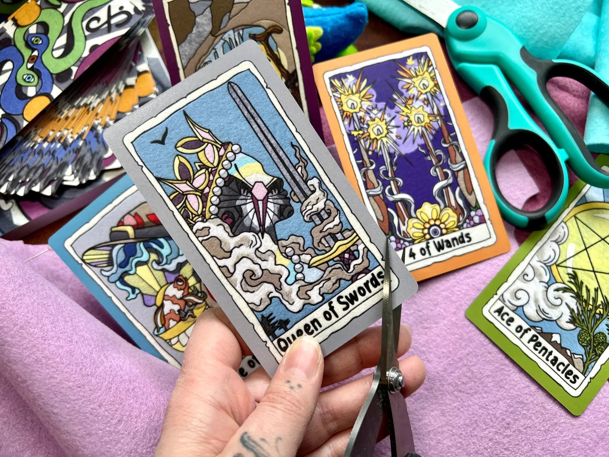 Colorful tarot cards with a hand holding 'Queen of Swords' card, scissors, and other cards in the background.