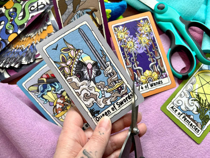 Colorful tarot cards with a hand holding 'Queen of Swords' card, scissors, and other cards in the background.