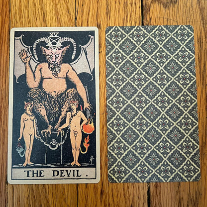 Tarot card featuring 'The Devil' with a patterned back on a wooden surface