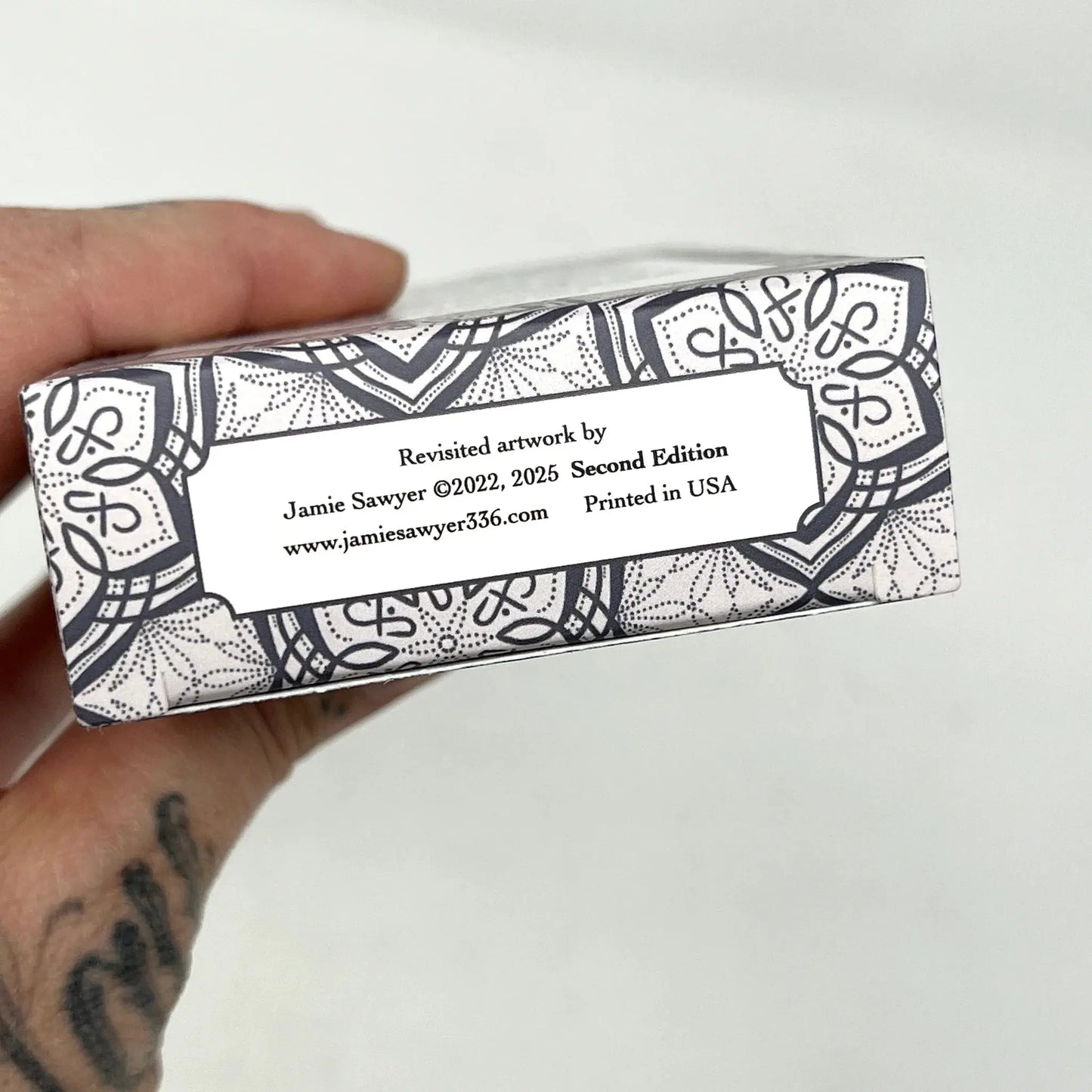 Hand holding a box with decorative patterns and text on a white  Jamie Sayer 1909 redux background