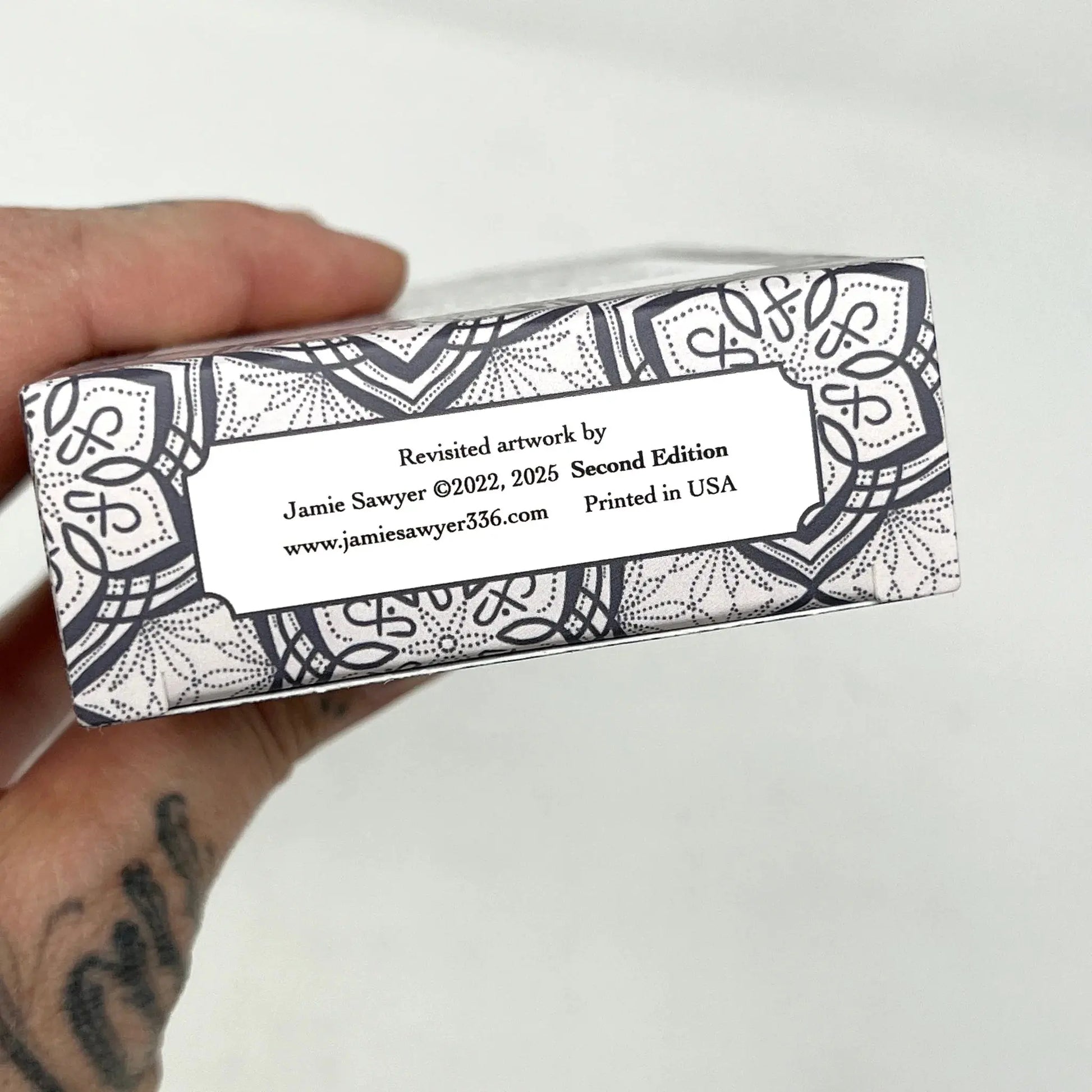 Hand holding a box with decorative patterns and text on a white  Jamie Sayer 1909 redux background