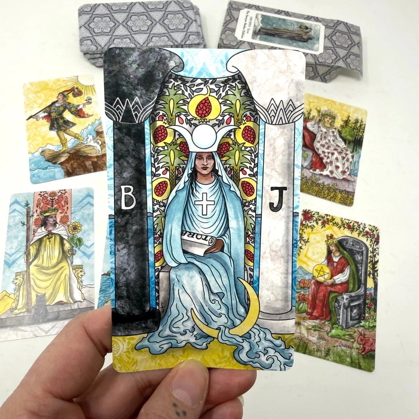 Colorful tarot card held by a hand with other tarot cards in the background. Jamie Sawyer 1909 redux
