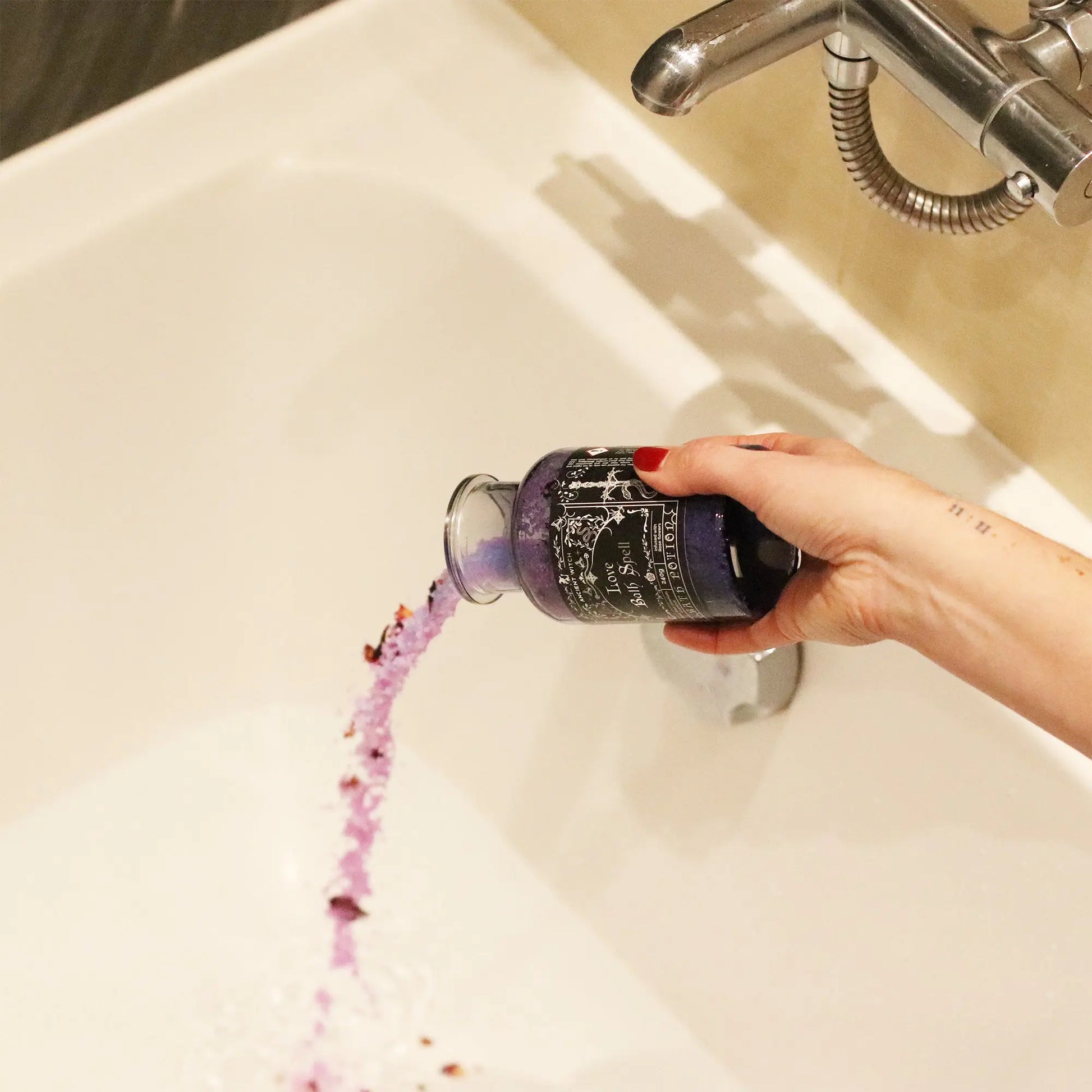 Person pouring purple bath salts from a bottle into a bathtub.