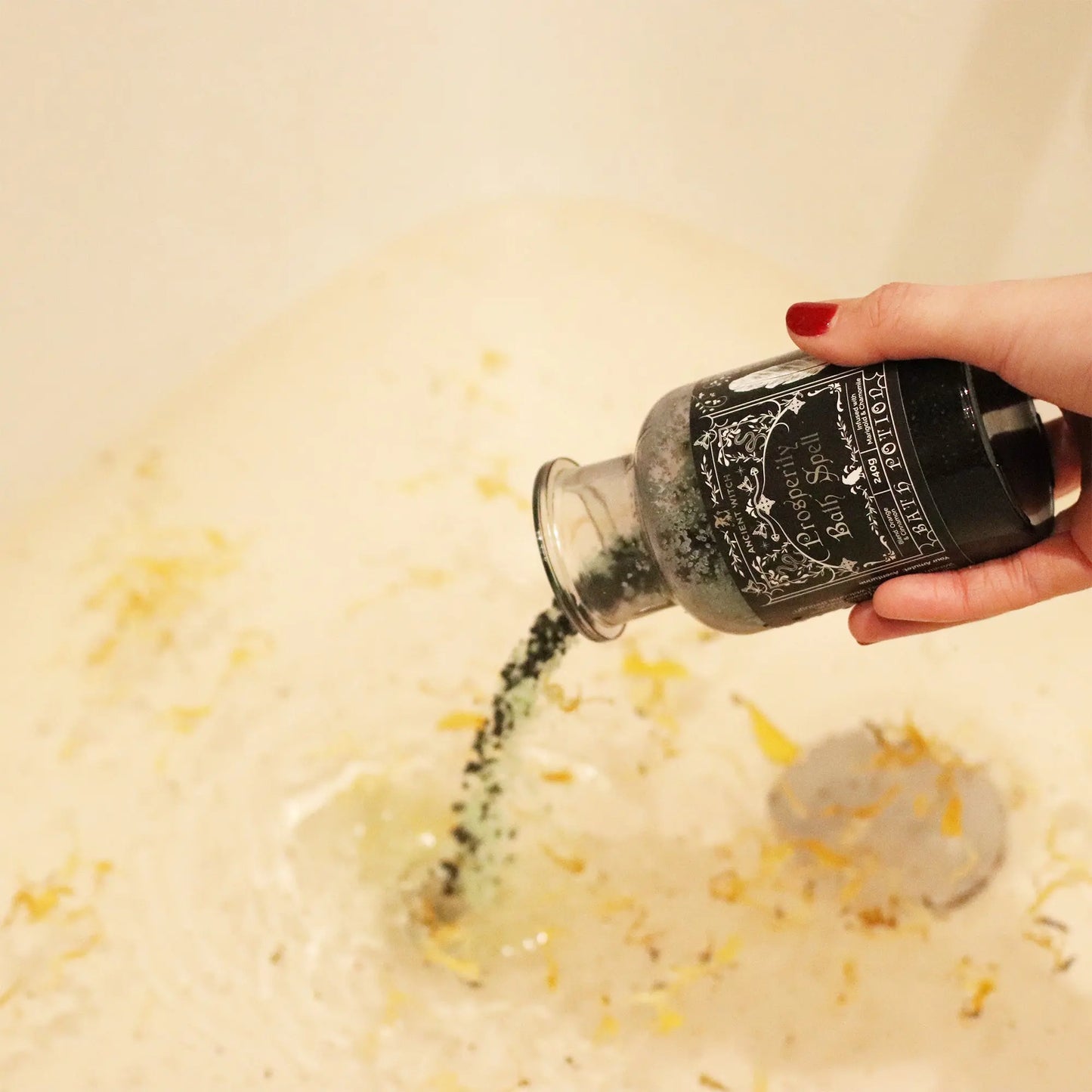 Person pouring a black bath bomb into a bathtub filled with water and yellow bath salts.
