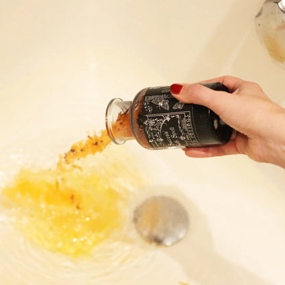 Hand holding a bottle over a sink with water and soap bubbles.