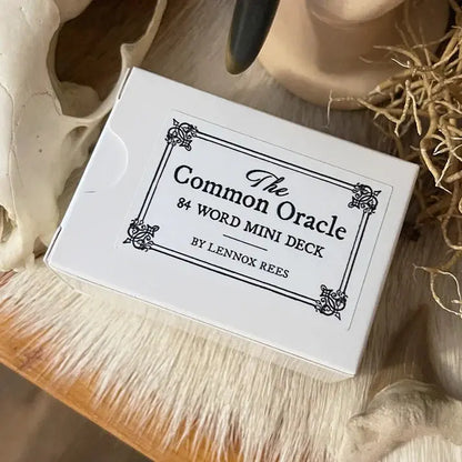 White card deck box with 'The Common Oracle' text on a wooden surface.