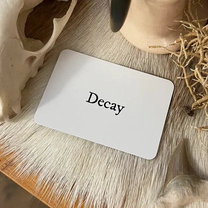 Card with 'Decay' text on a wooden surface with natural elements