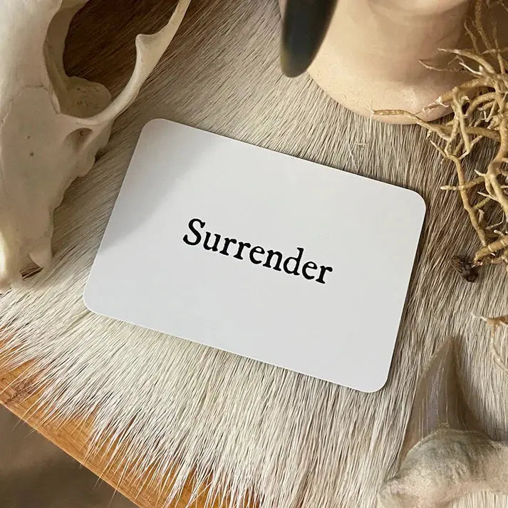 Card with 'Surrender' text on a wooden surface with natural elements