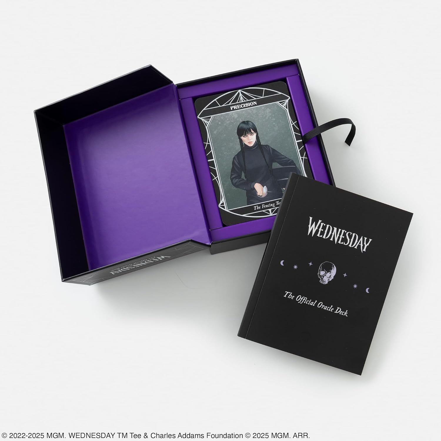 Open box containing a 'Wednesday' themed product with a card and book on a white background.